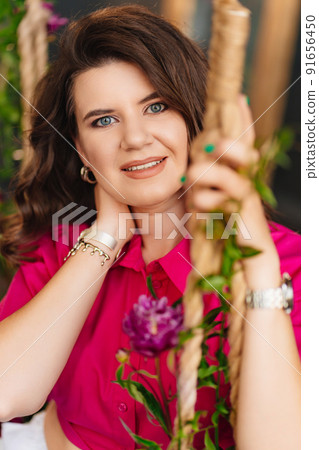 an attractive woman in a pink blouse with peonies on the swing. 91656450
