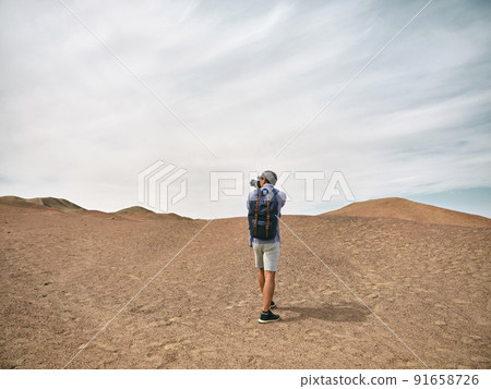 asian male backpacker landscape photographer taking a photo on a hill, rear view 91658726
