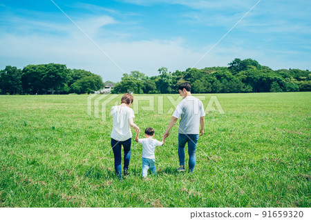 父母和孩子手牽手走在陽光明媚的綠地的背影 父母和孩子手牽手走在陽光明媚的綠地的背影 91659320