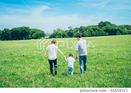 父母和孩子手牽手走在陽光明媚的綠地的背影 父母和孩子手牽手走在陽光明媚的綠地的背影 91659321