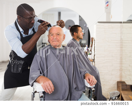 Elderly man getting haircutting from African barber Elderly man getting haircutting from African barber 91660015