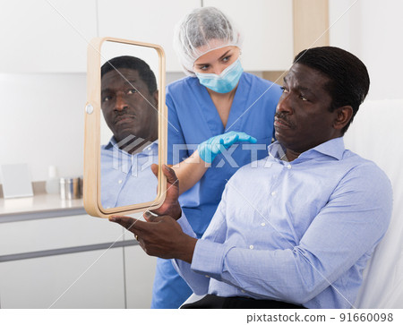 Man looking at mirror while beautician examining his face in cosmetology office 91660098