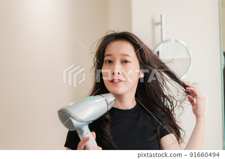 Young woman drying her hair with a hair dryer 91660494