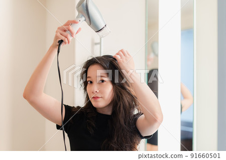 Young woman drying her hair with a hair dryer 91660501