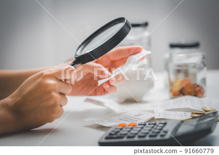 Woman hand holding magnifying glass to check receipts to calculate expenses. Concept of checking personal income and expenses. 91660779