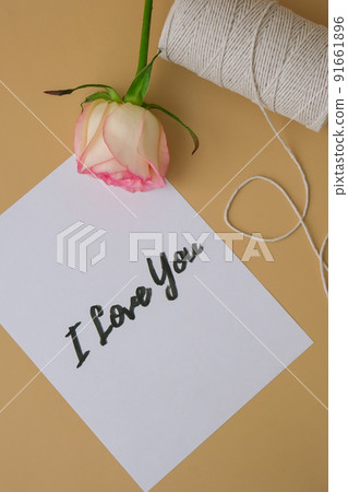 I LOVE YOU text on paper note. Delicate pink roses with spool of white cotton rope on beige background. Minimal trendy composition. Romantic pastel pink rose flowers. Neutral earth tones. Greeting I LOVE YOU text on paper note. Delicate pink roses with spool of white cotton rope on beige background. Minimal trendy composition. Romantic pastel pink rose flowers. Neutral earth tones. Greeting 91661896