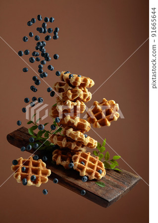 Waffles with fresh blueberries in motion. 91665644