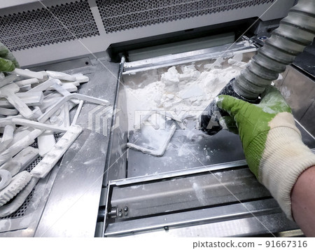 A man working with a working vacuum cleaner to clean the white powder of polyamide from a model printed on a 3D printer inside a 3D printer. Cleaning objects printed on an industrial powder 3D printer A man working with a working vacuum cleaner to clean the white powder of polyamide from a model printed on a 3D printer inside a 3D printer. Cleaning objects printed on an industrial powder 3D printer 91667316