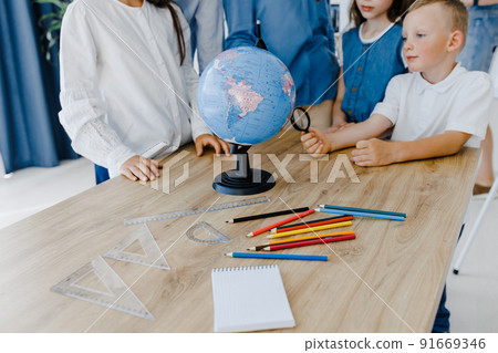 Teacher and children in class are looking at globe, teacher helps explain the lesson to the children in the class at a desk. 91669346