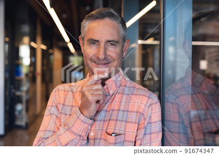 Portrait of smiling mature caucasian businessman with hand on chin in creative office Portrait of smiling mature caucasian businessman with hand on chin in creative office 91674347