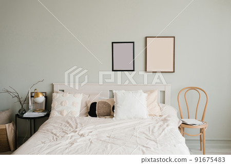 Double bed with white linens and beige pillows in a bright Scandinavian bedroom, mockup paintings above the bed 91675483