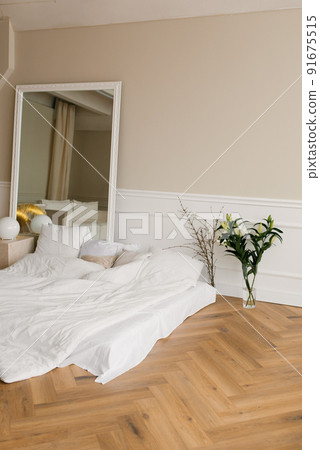 Bright and spacious bedroom with a Scandinavian-style bed on the floor. Bouquet of lilies in a glass vase 91675515