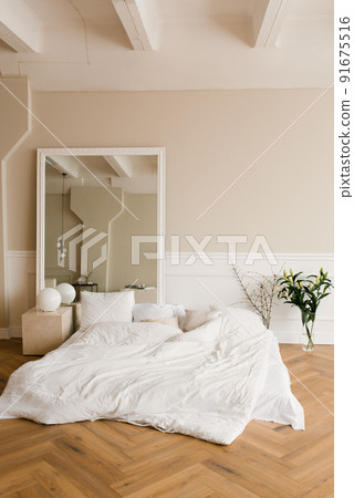A cozy bed on the floor, a large mirror in a classic modern bedroom. Interior of the house 91675516