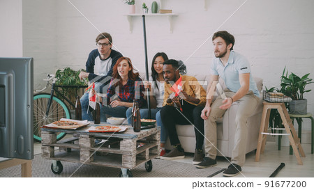 Multi ethnic group of friends sports fans with Swiss national flags watching hockey championship on TV together cheering up their favourite team at home indoors 91677200