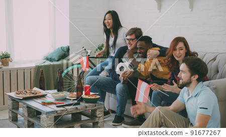 Happy friends with Austrian flags watching sports championship on TV together at home indoors and happy about winning of favourite team 91677267