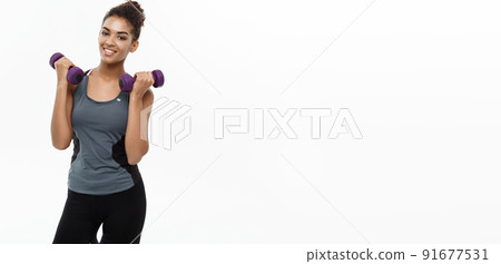 Healthy and Fitness concept - Beautiful American African lady in fitness clothes workout with dumbbell. Isolated on white background. 91677531