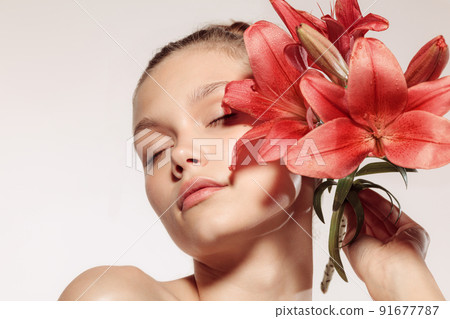 Beauty portrait of charm young girl with flower isolated over white studio background. Cosmetics, natural beauty and aesthetic cosmetology concept. 91677787
