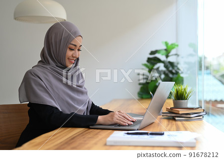 Pleasant Muslim woman using typing business email, searching information on laptop computer Pleasant Muslim woman using typing business email, searching information on laptop computer 91678212