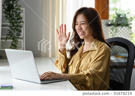 Cheerful young woman looking at her laptop screen, communicating by video conference on laptop computer Cheerful young woman looking at her laptop screen, communicating by video conference on laptop computer 91678219