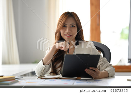 Gorgeous asian female entrepreneur holding clipboard and looking confidently to camera Gorgeous asian female entrepreneur holding clipboard and looking confidently to camera 91678225