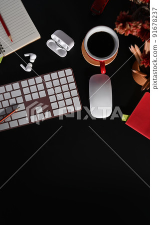 Black wooden office with wireless keyboard, coffee cup, earphone and flower pot 91678237