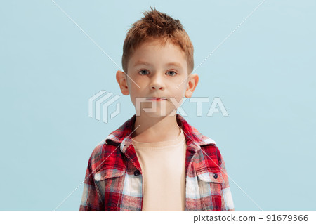 Portrait of little boy, child in checkered shirt looking at camera, posing isolated on blue background Portrait of little boy, child in checkered shirt looking at camera, posing isolated on blue background 91679366