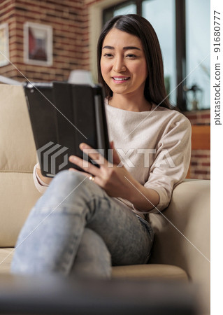 Beautiful young chinese woman using digital tablet at home, connecting internet web 3.0 smiling while sitting on couch entertainment device, browsing internet wireless device computer tablet using Beautiful young chinese woman using digital tablet at home, connecting internet web 3.0 smiling while sitting on couch entertainment device, browsing internet wireless device computer tablet using 91680777