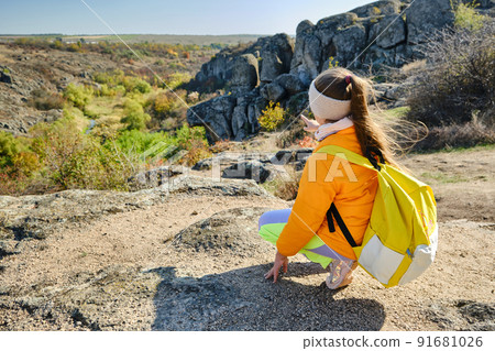little girl with a backpack standing on a mountain top at the day time little girl with a backpack standing on a mountain top at the day time 91681026