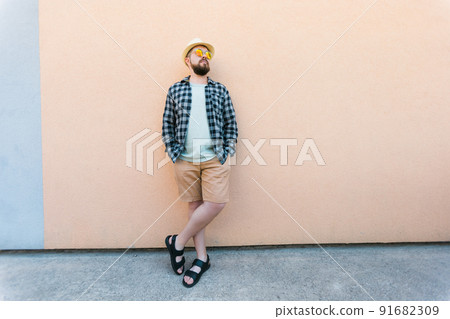 Bearded man in summer clothes and hat stand over beige wall on street city urban and travel concept - copy space and empty space for advertising Bearded man in summer clothes and hat stand over beige wall on street city urban and travel concept - copy space and empty space for advertising 91682309