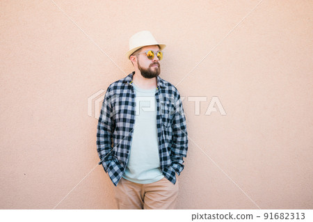 Bearded man in summer clothes and hat stand over beige wall on street city urban and travel concept - copy space and empty space for advertising Bearded man in summer clothes and hat stand over beige wall on street city urban and travel concept - copy space and empty space for advertising 91682313
