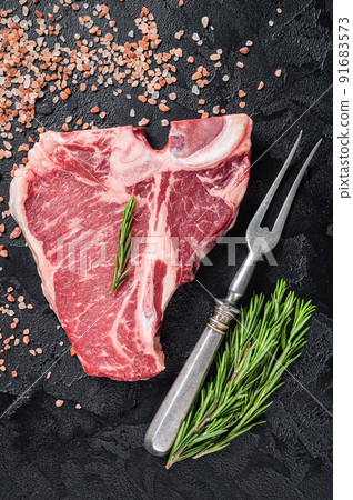 Raw T bone beef meat steak, porterhouse steak on butcher table with rosemary. Black background. Top view 91683573