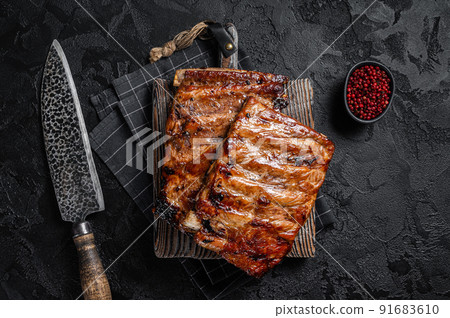 Stack of grilled pork ribs in BBQ sauce on a chopping board. Black background. Top view Stack of grilled pork ribs in BBQ sauce on a chopping board. Black background. Top view 91683610