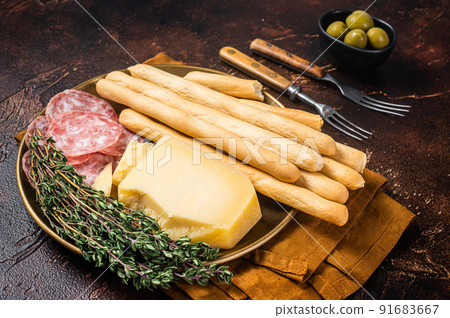 Appetizer plate with antipasti snacks grissini bread sticks, salami, olives and parmesan cheese. Dark bakground. Top view 91683667