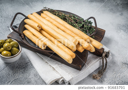 Italian grissini bread sticks in steel tray with herbs. White bakground. Top view 91683701