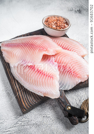 Raw white fish tilapia, uncooked fillet in kitchen tray with herbs. Gray background. Top view. 91683702