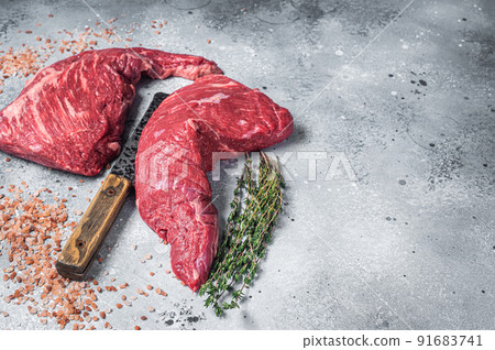Unccoked tri-tip triangle roast, raw bottom sirloin steak on buther table with meat cleaver. Gray background. Top view. Copy space Unccoked tri-tip triangle roast, raw bottom sirloin steak on buther table with meat cleaver. Gray background. Top view. Copy space 91683741