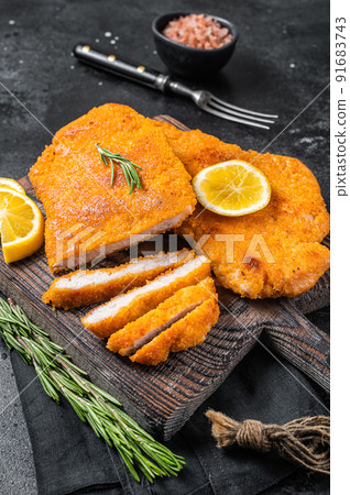 Fried sliced weiner schnitzel on a wooden board with herbs. Black background. Top view 91683743