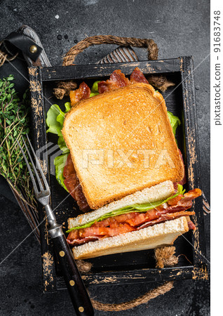 Homemade toasted BLT sandwich with bacon, tomato and lettuce in wooden tray. Black background. Top view Homemade toasted BLT sandwich with bacon, tomato and lettuce in wooden tray. Black background. Top view 91683748