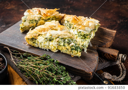 Spanakopita Greek Pie with Spinach and Cheese on wooden board. Dark background. Top view Spanakopita Greek Pie with Spinach and Cheese on wooden board. Dark background. Top view 91683850