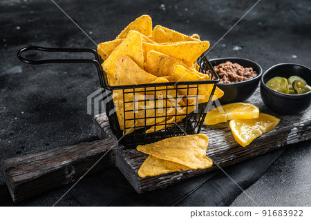 Mexican nachos corn chips with Chili con carne and jalapeno in a basket. Black background. Top view Mexican nachos corn chips with Chili con carne and jalapeno in a basket. Black background. Top view 91683922