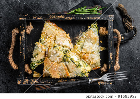 Spinach pie pieces, Spanakopita Greek Pie in wooden tray. Black background. Top view Spinach pie pieces, Spanakopita Greek Pie in wooden tray. Black background. Top view 91683952