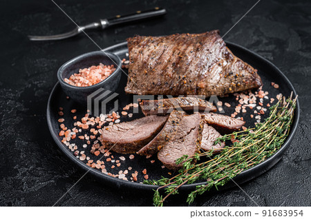 Barbecue dry aged wagyu Tri Tip beef steak on a plate with pink salt. Black background. Top view Barbecue dry aged wagyu Tri Tip beef steak on a plate with pink salt. Black background. Top view 91683954