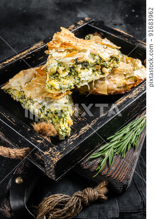 Spinach pie pieces, Spanakopita Greek Pie in wooden tray. Black background. Top view Spinach pie pieces, Spanakopita Greek Pie in wooden tray. Black background. Top view 91683962