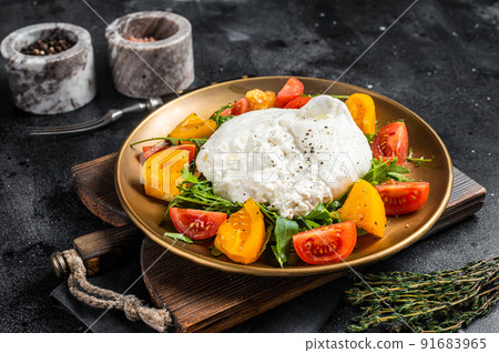 Burrata cheese with cherry tomatoes and fresh arugula in a plate. Black background. Top view 91683965