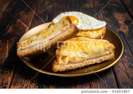 French toasts Croque monsieur and croque madame, grilled sandwiches on brioch bread with sliced ham, melted emmental cheese and egg. Wooden background. Top view 91683967