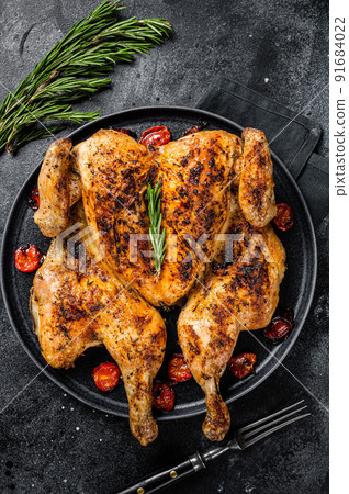 Tobacco whole chicken on plate with herbs and tomato. Black background. Top view Tobacco whole chicken on plate with herbs and tomato. Black background. Top view 91684022