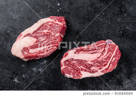 Raw chuck eye roll steaks, premium beef meat on a butcher board. Black background. Top view Raw chuck eye roll steaks, premium beef meat on a butcher board. Black background. Top view 91684084