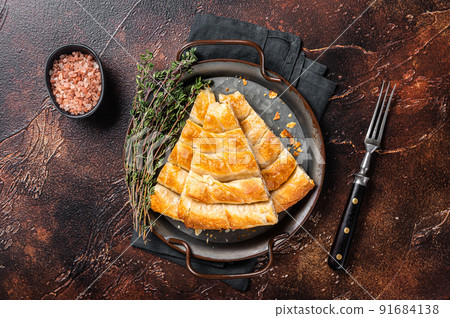 Slices of baked Round Borek cheese pie in kitchen tray with herbs. Dark background. Top view Slices of baked Round Borek cheese pie in kitchen tray with herbs. Dark background. Top view 91684138