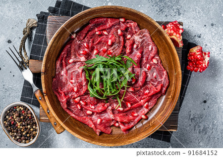 Classic beef meat carpaccio with arugula and pomegranate seeds. Gray background. Top view 91684152