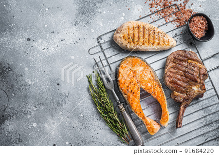 Set of bbq grilled meat steaks salmon, beef and turkey on a grill. Gray background. Top view. Copy space Set of bbq grilled meat steaks salmon, beef and turkey on a grill. Gray background. Top view. Copy space 91684220